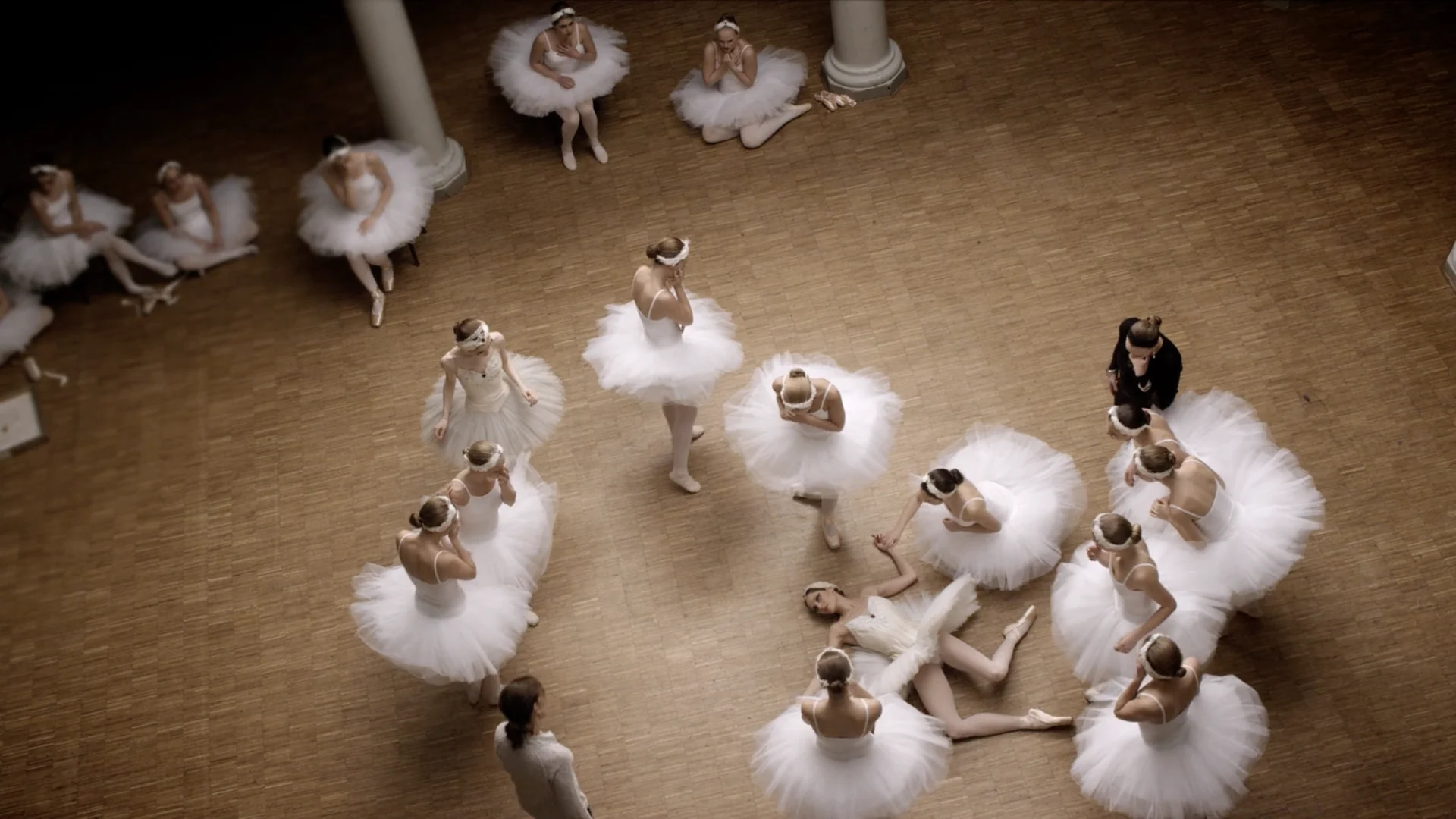 Seen from above, dancers in white tutus scattered across a wooden floor