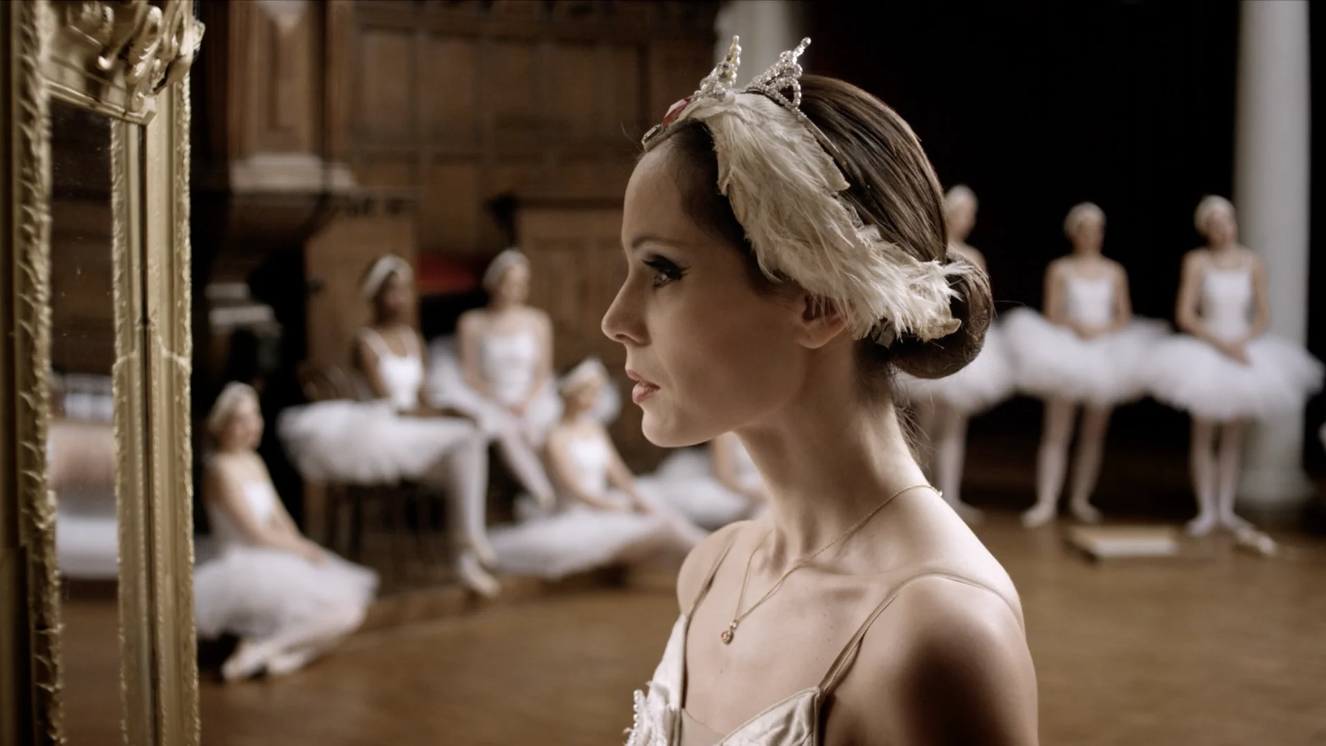 Igone de Jongh in profile beside a gilded mirror, dancers in a row behind her