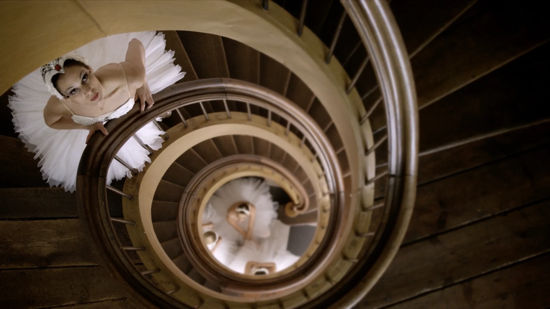 Looking down a spiral staircase at a ballerina leaning over the banister