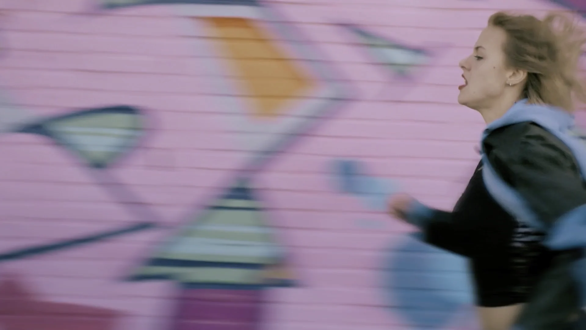 Susan Radder runs past a pink graffiti wall, her hood flying