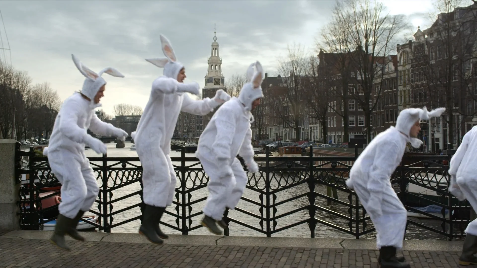 A group of white rabbits jumps on a canal bridge in Amsterdam, in Pretending As Always