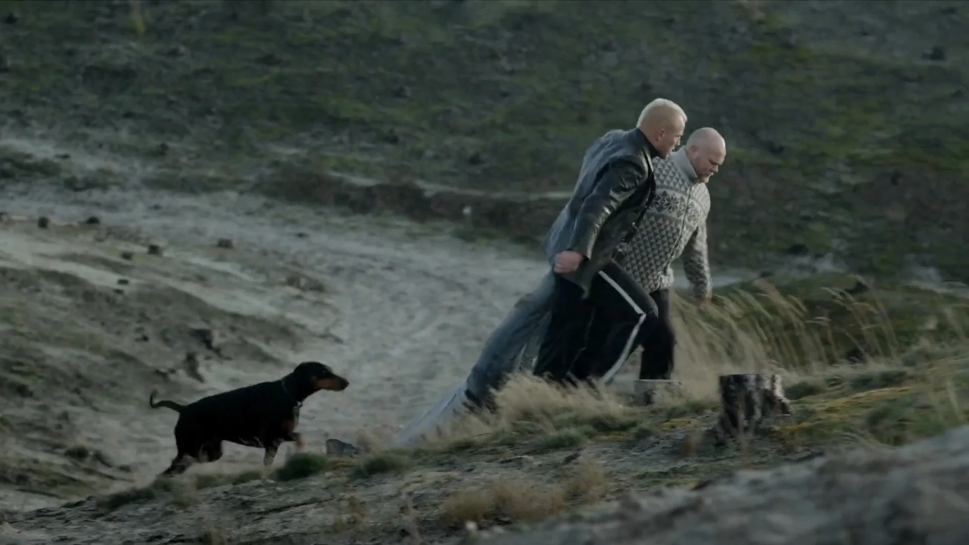 Two men and a dog climb a sandy path in the dunes, in The Good Life