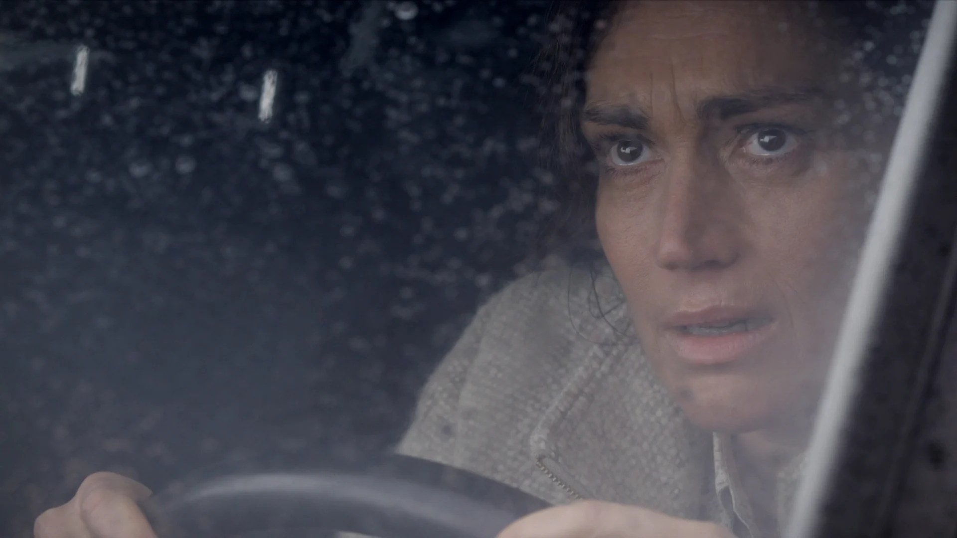A woman drives through the rain at night, her face tense, in Kill
