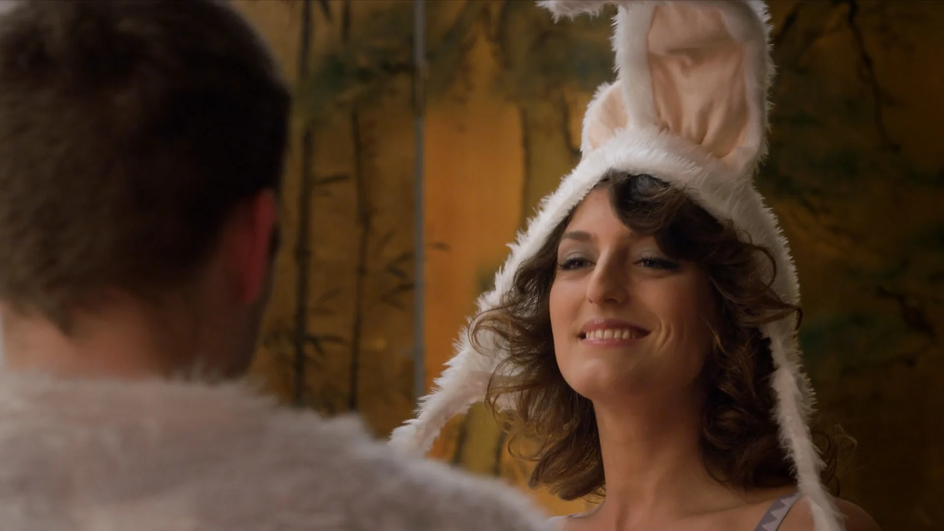 A woman in a white rabbit hood smiles at a man, in Pretending As Always