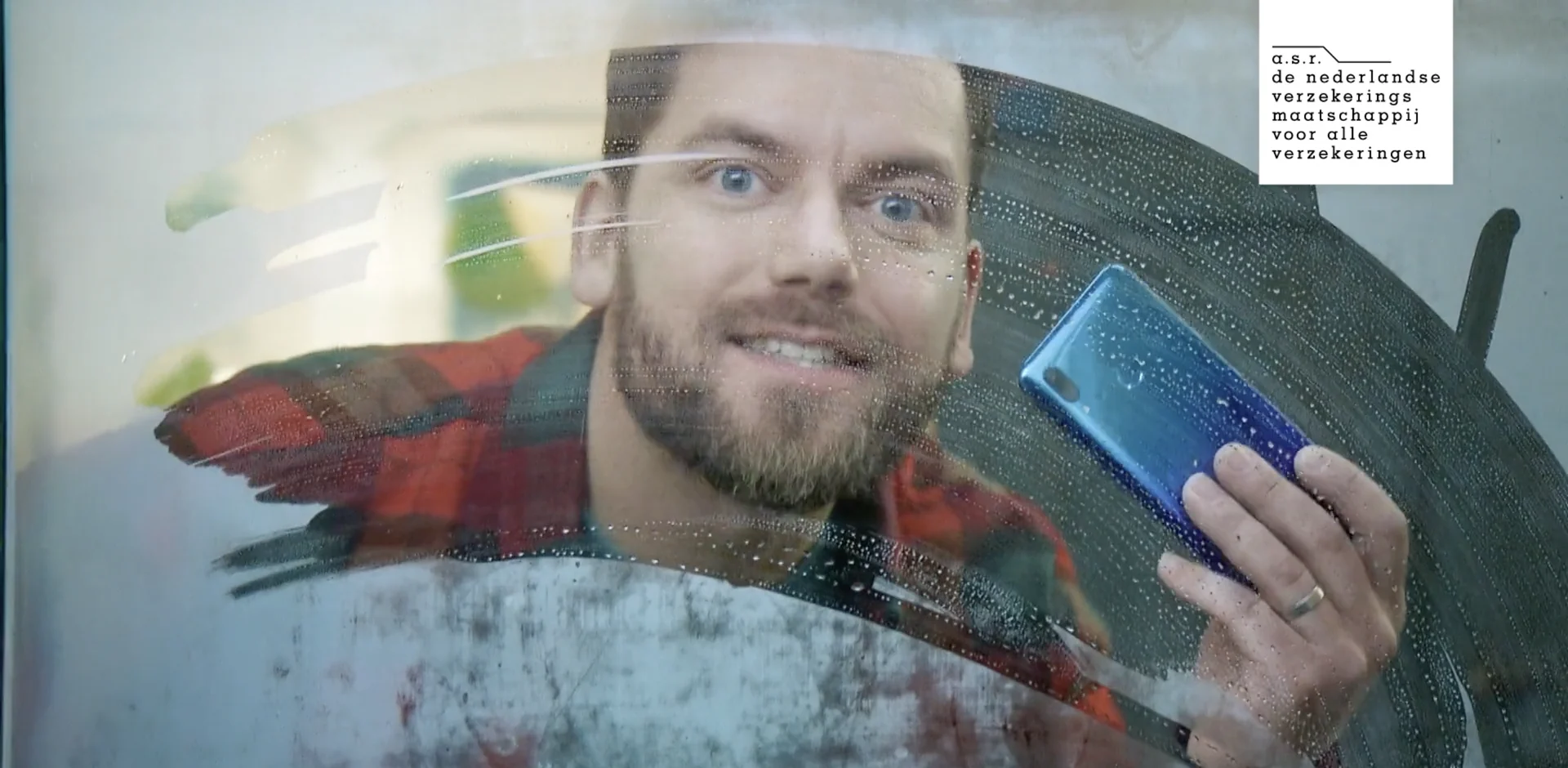 A man with a phone wipes a fogged window clean