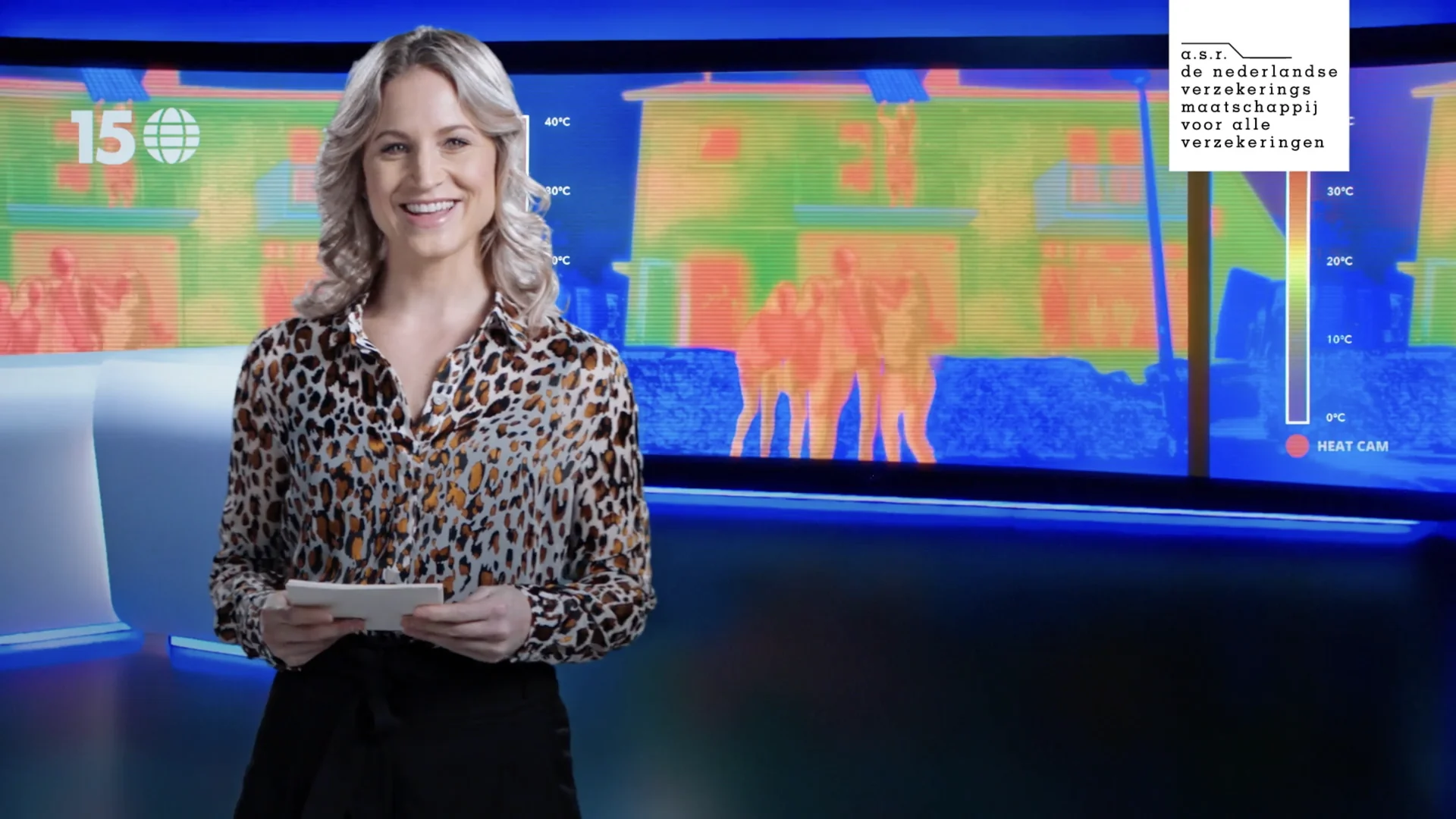 A weather presenter in a studio in front of a heat camera image of houses