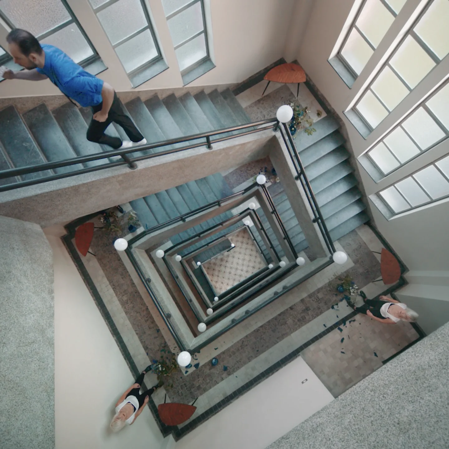 A man in a blue shirt looks over the banister, the stairwell spiralling down beneath him