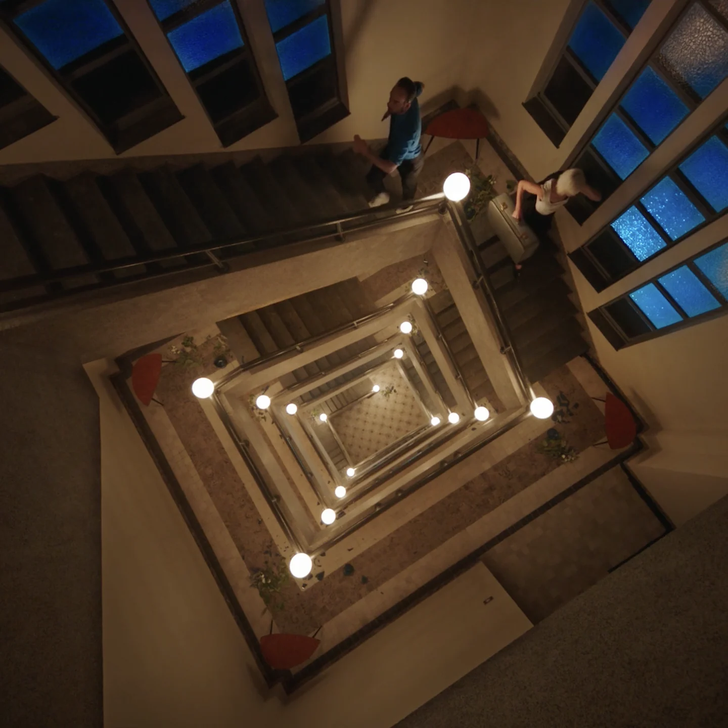 The stairwell at night, lamps circling down into the dark like a tunnel