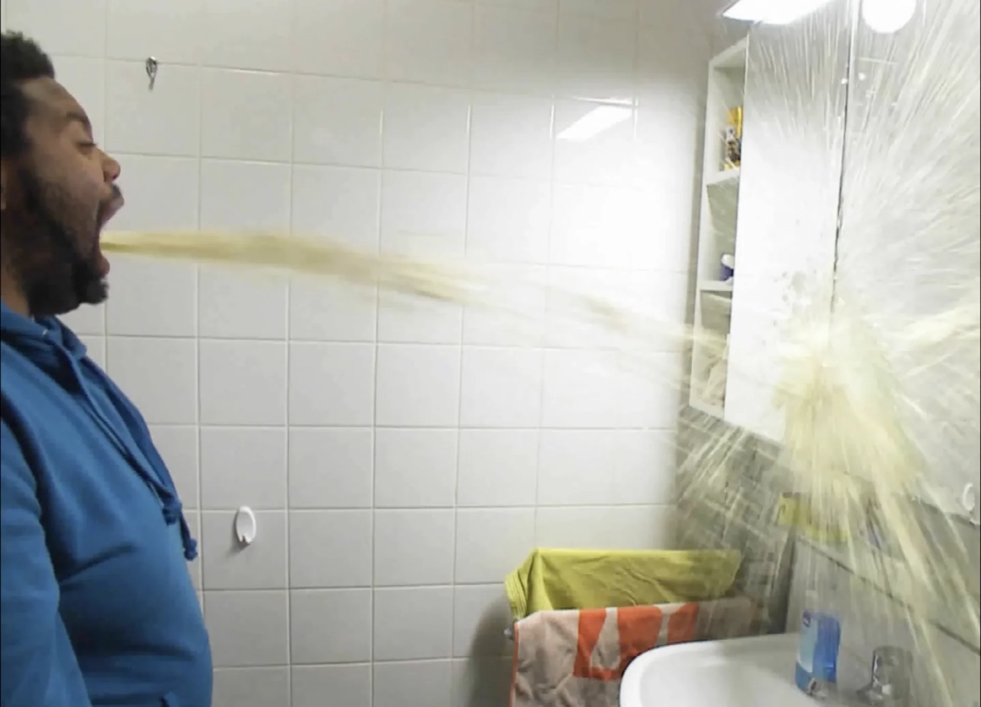 A man sprays a jet of liquid out of his mouth across a bathroom