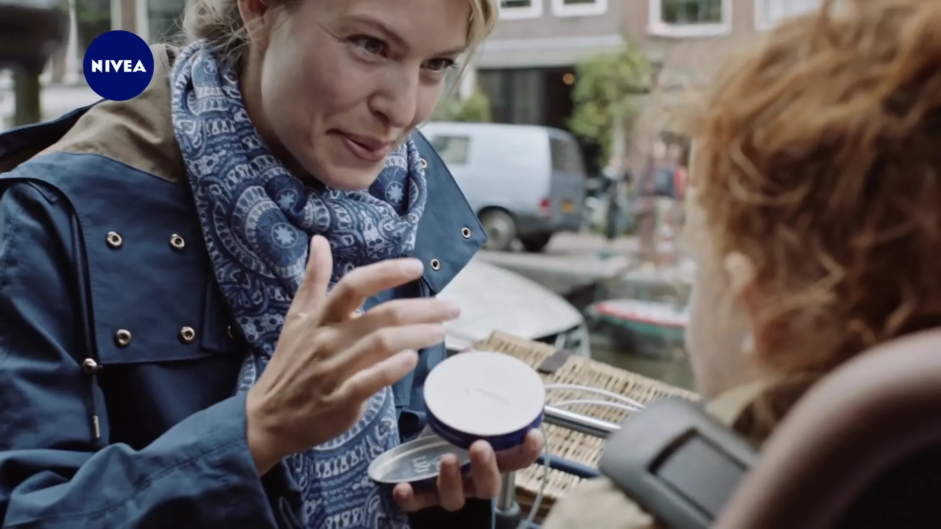 A mother rubs Nivea cream into her hands beside an Amsterdam canal while her child watches