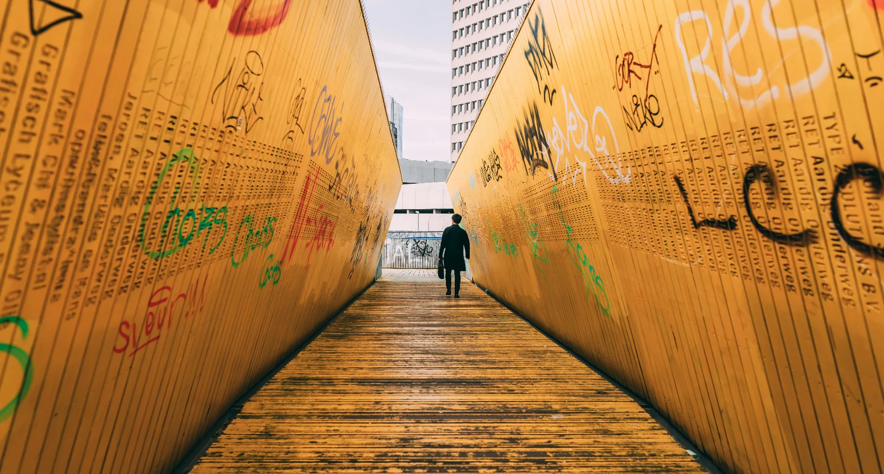 A person walking through an orange tunnel with graffiti