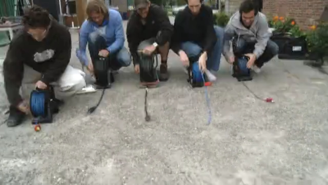 Five crew members crouch on the gravel, each unrolling a cable reel