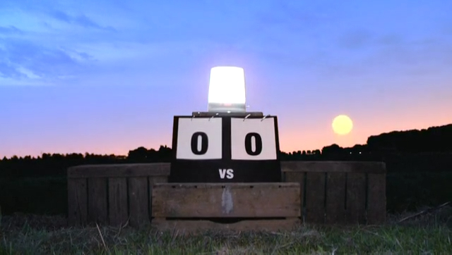 A scoreboard reading nil nil with a lamp on top, as the sun rises behind it