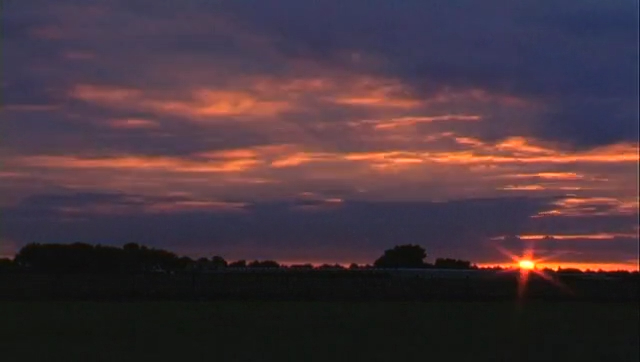 The sun sets over a flat Dutch field under an orange sky