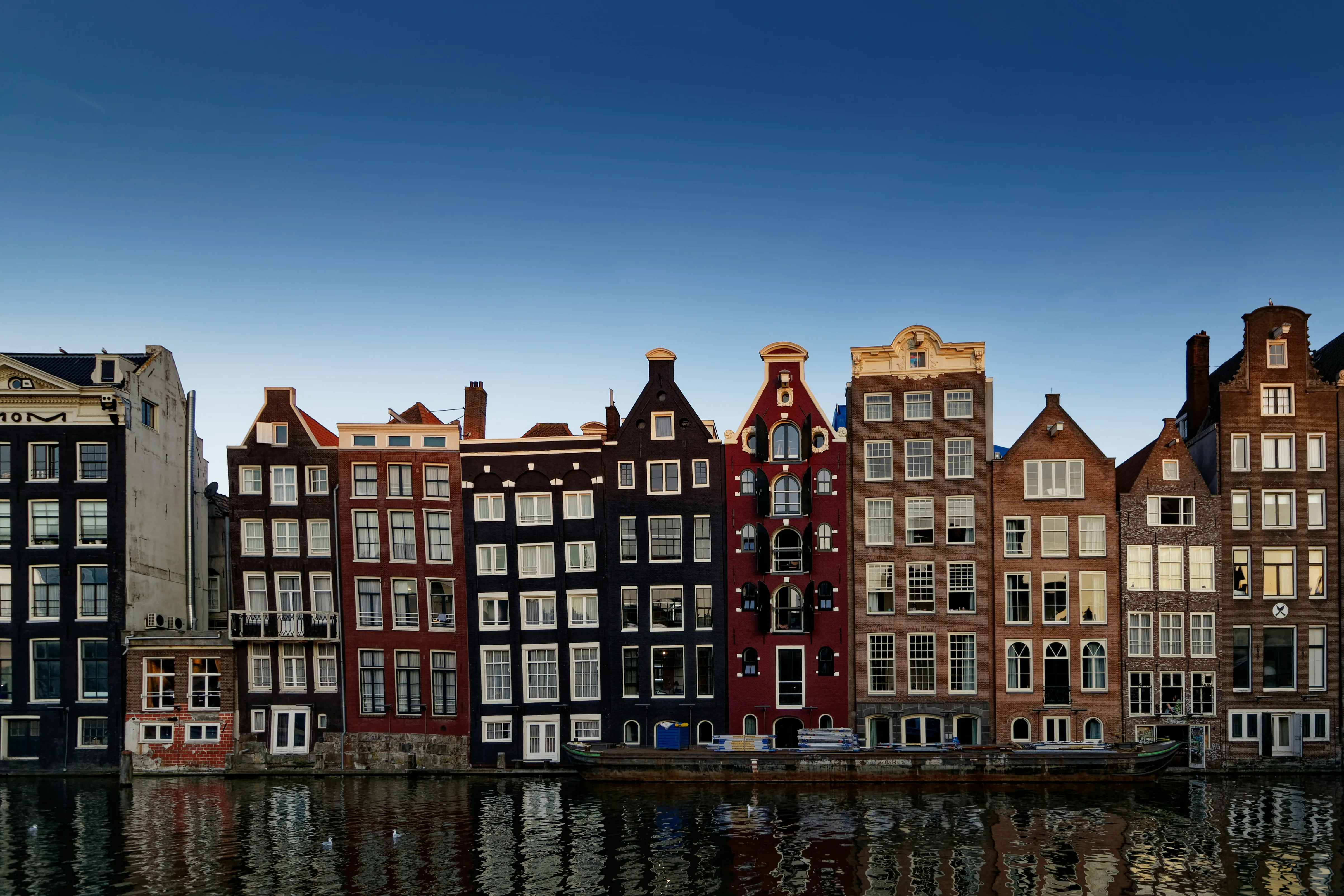A row of tall narrow canal houses on the Damrak, reflected in the water