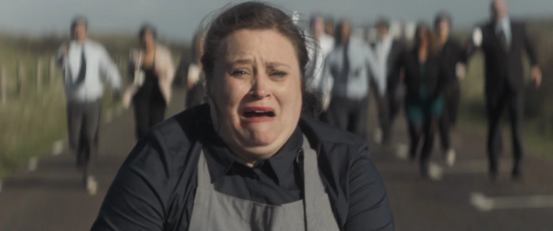 A woman in an apron cries as a crowd runs up behind her