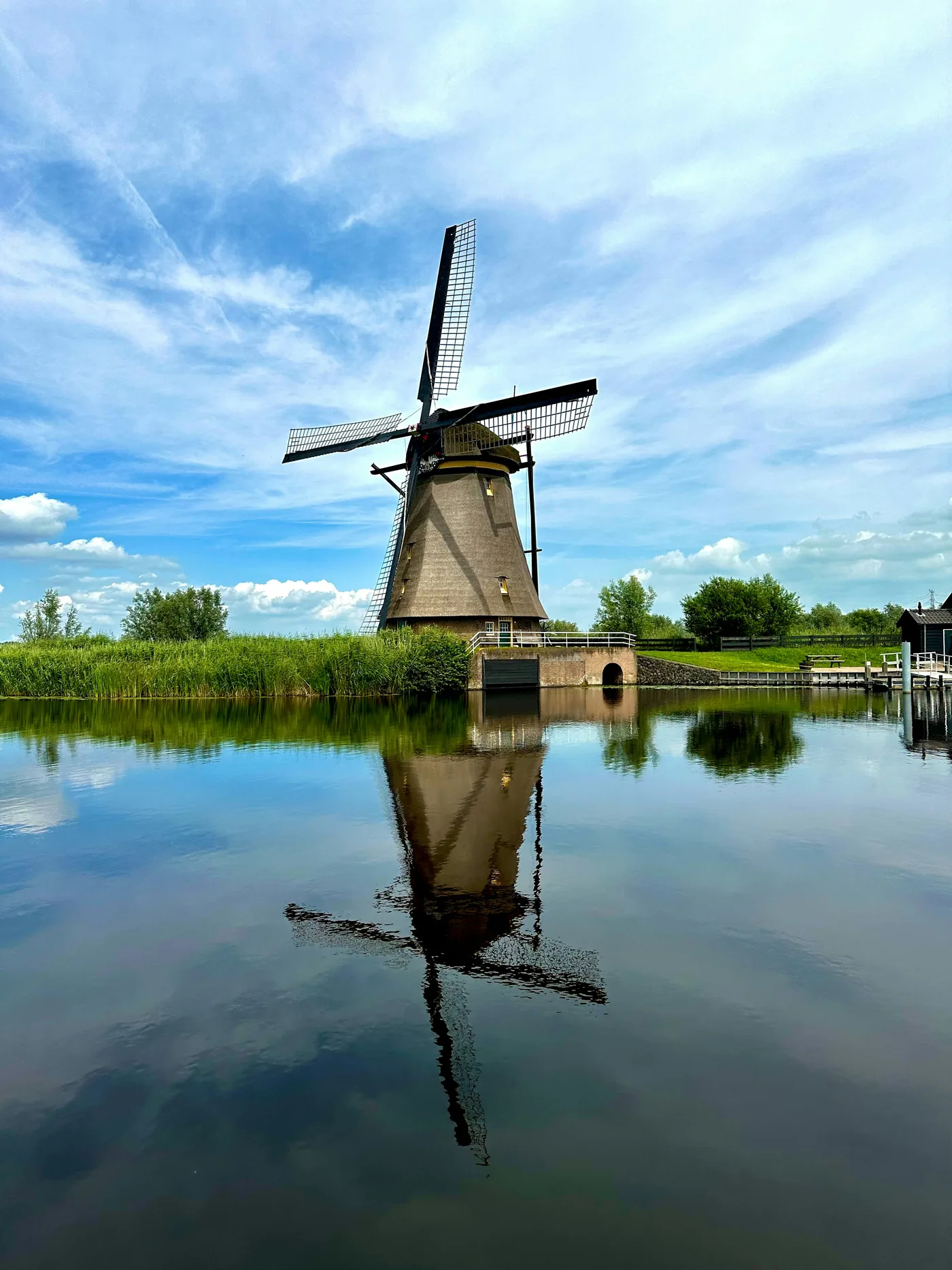 A thatched mill beside reeds, reflected in a polder canal