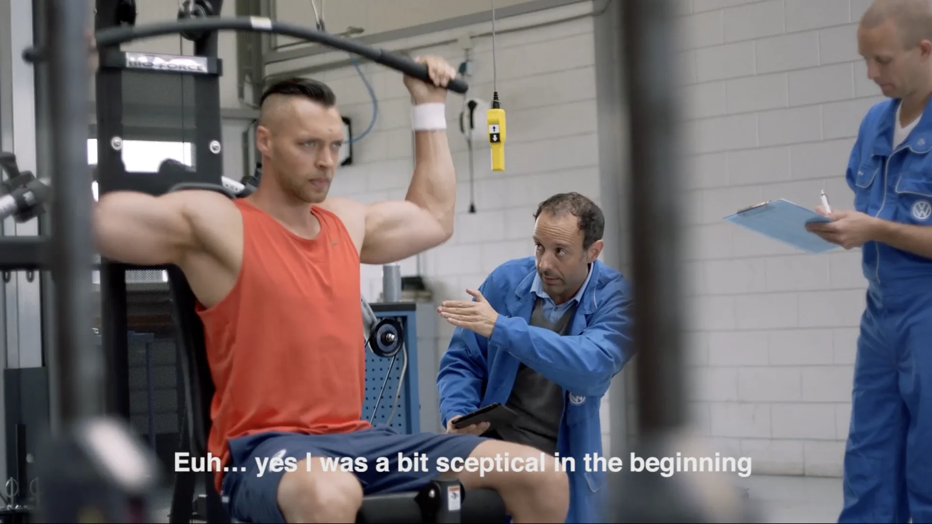 An athlete trains on a chest press while engineers in blue overalls take notes