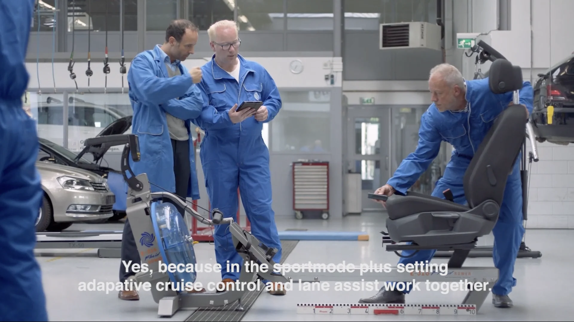 Engineers in blue overalls test a car seat next to a rowing machine